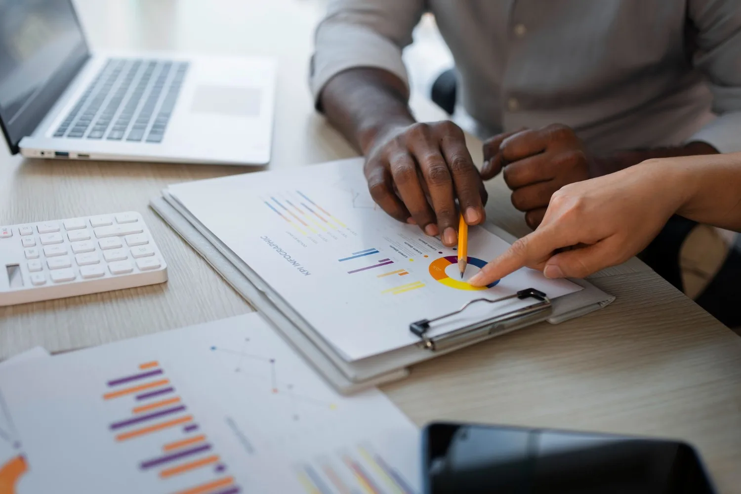 Two people pointing at charts on a printed KPI report beside a calculator