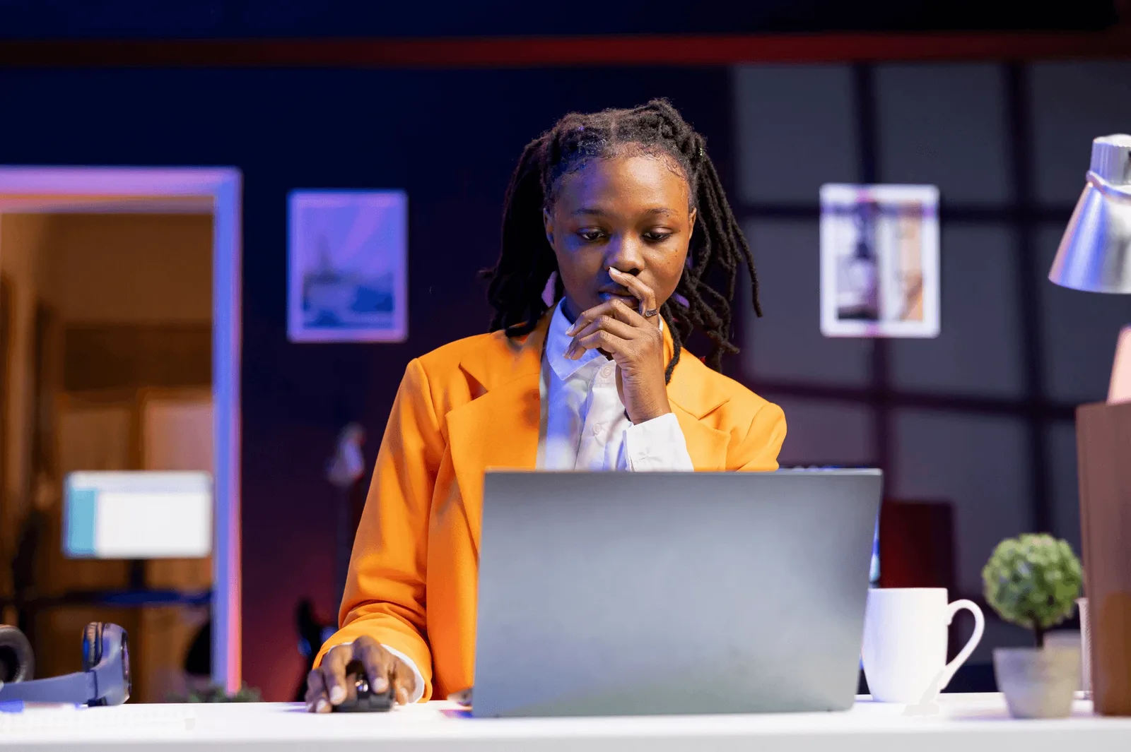 A professional in an orange blazer reviewing work on a laptop