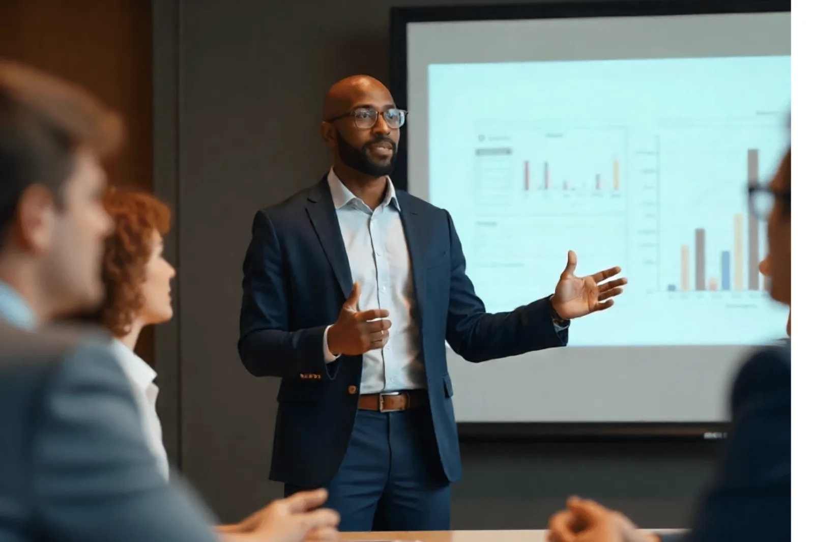A man in a navy suit presenting bar charts to a meeting